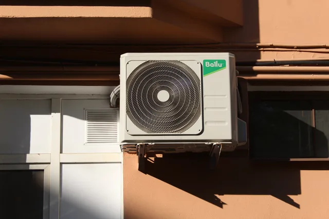 A Ballu air conditioner condenser unit mounted on a building exterior, showcasing modern HVAC technology. Hvilke sikkerhedskrav gælder for varmepumper og ventilation?